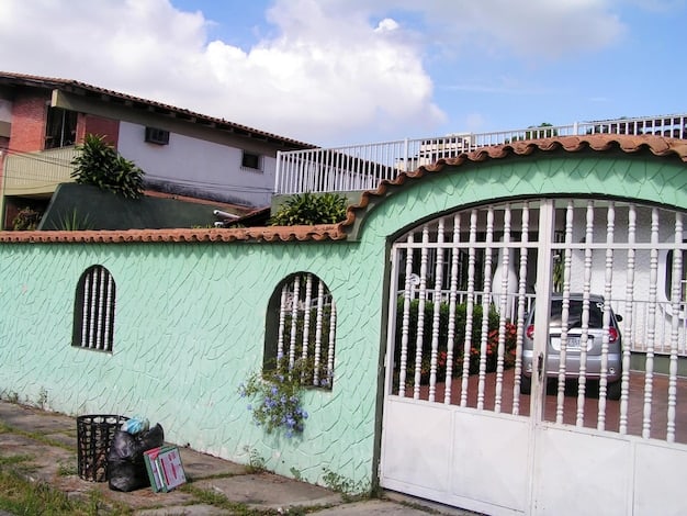 Exterior view of a modest, well-maintained brick house in a suburban neighborhood in Colombia. The house has a small garden and a welcoming front porch, illustrating a typical pre-owned dwelling in the region.