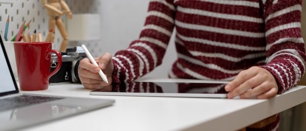 A person reviewing a credit report on a laptop, with a pen in hand and a calculator on the desk. The background shows a home office setting.