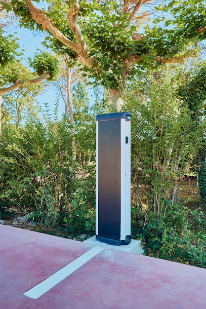 A close-up shot of an electric car charging station surrounded by lush green vegetation in Colombia. The charging station is modern and user-friendly.