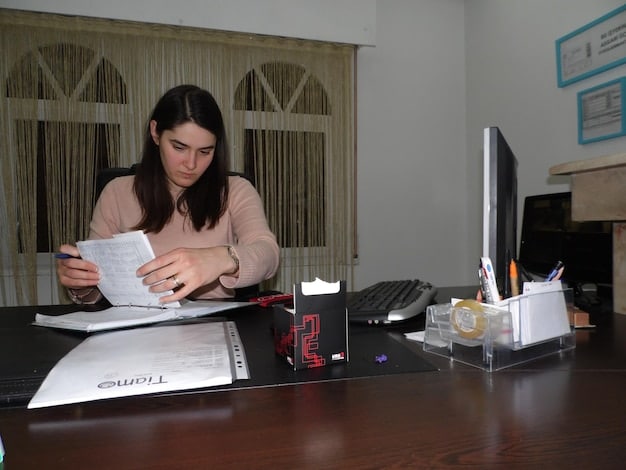 A Colombian worker is reviewing documents related to a vehicle loan application at their home office. The scene should display organization.