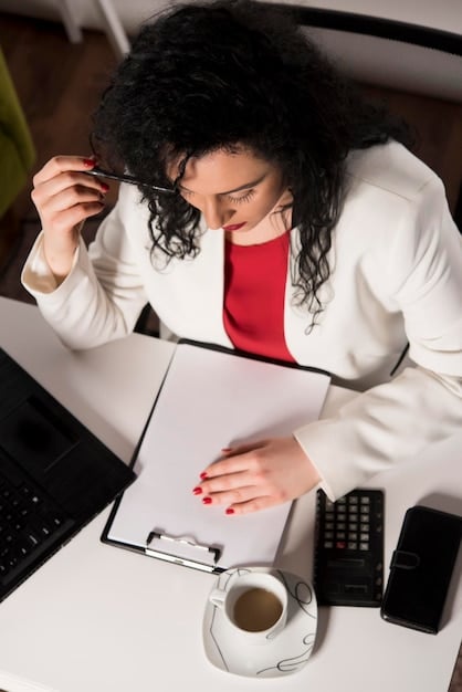 A person sitting at a desk, reviewing financial documents with a pen in hand, and a laptop displaying a spreadsheet with loan details. The setting is well-lit and professional, suggesting careful financial planning