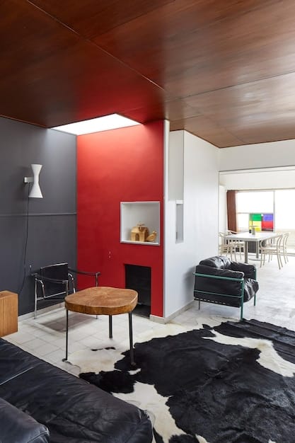 Interior shot of a modern living room in an Bogotá apartment. The room features large windows overlooking the city skyline, letting in plenty of natural light. The decor is minimalist with a neutral color palette, and a family can be seen spending time together.