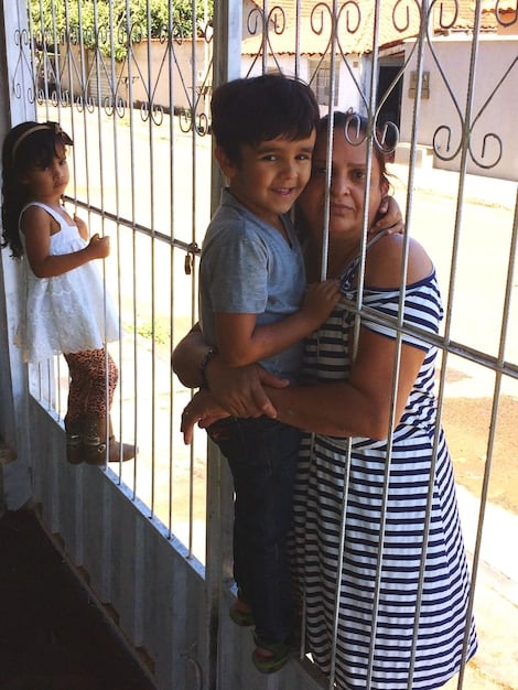 A family of three, including a mother, father, and child, standing happily in front of their new house in Colombia, holding keys and smiling at the camera.
